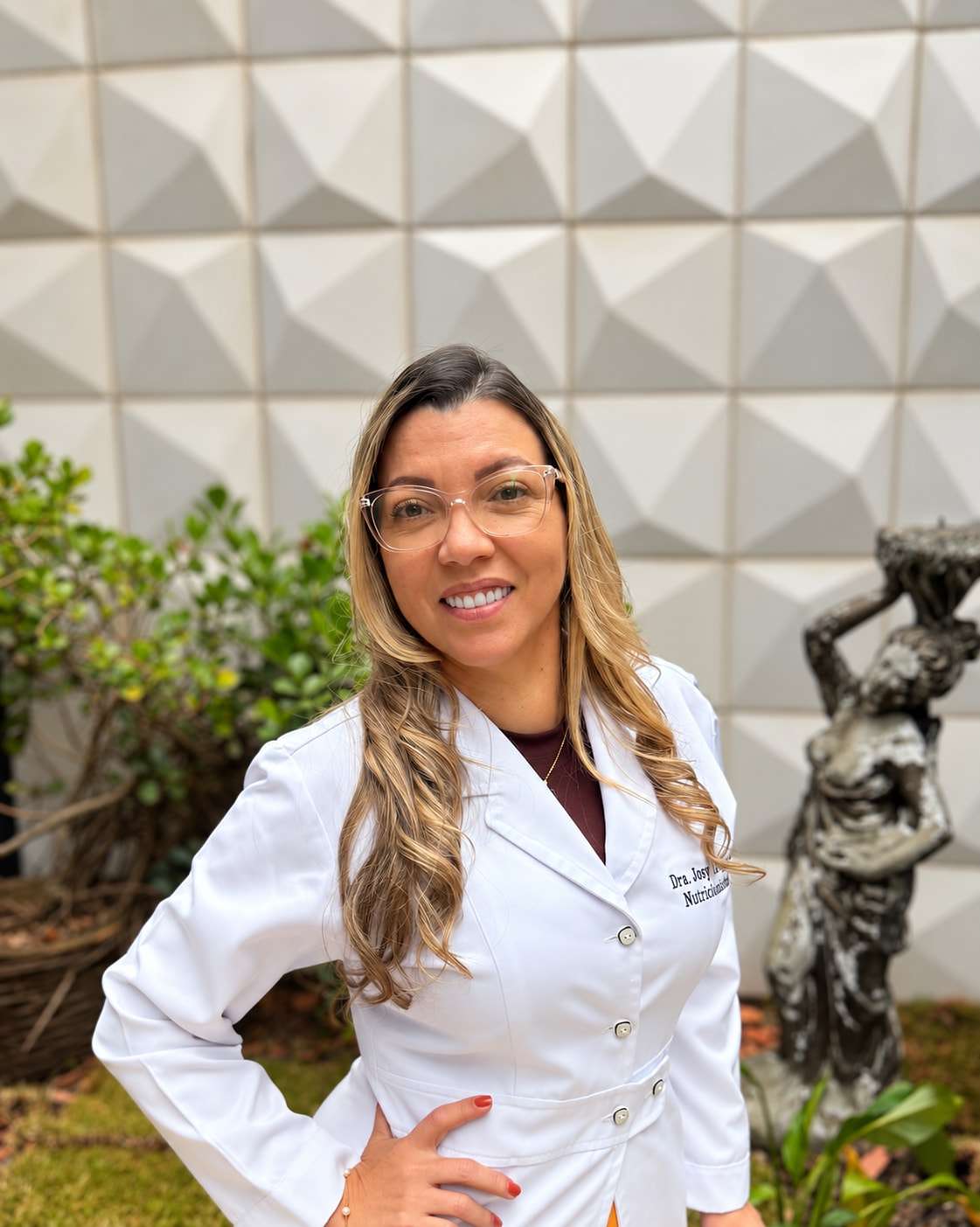 Dra. Josy Dantas, nutricionista em Jundiaí, de jaleco branco, em pé, sorrindo