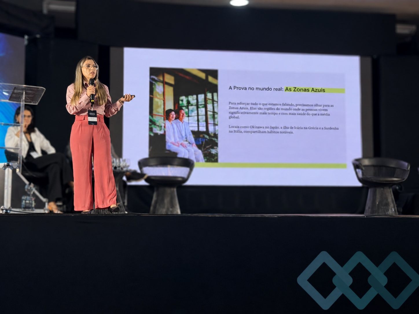 Dra. Josy Dantas no palco, falando ao microfone durante uma palestra sobre alimentação e saúde